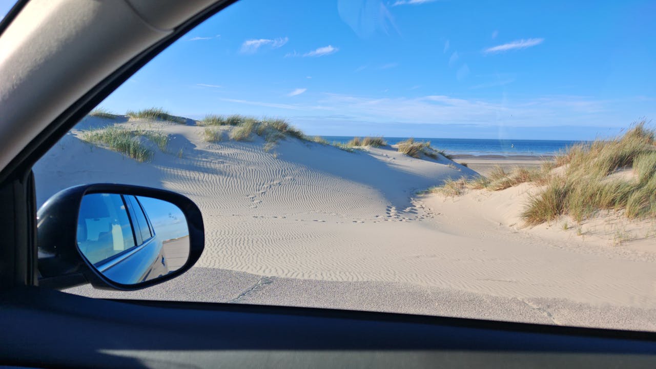 a picture taken from inside a car while parked at a beach, looking at the sand dunes.