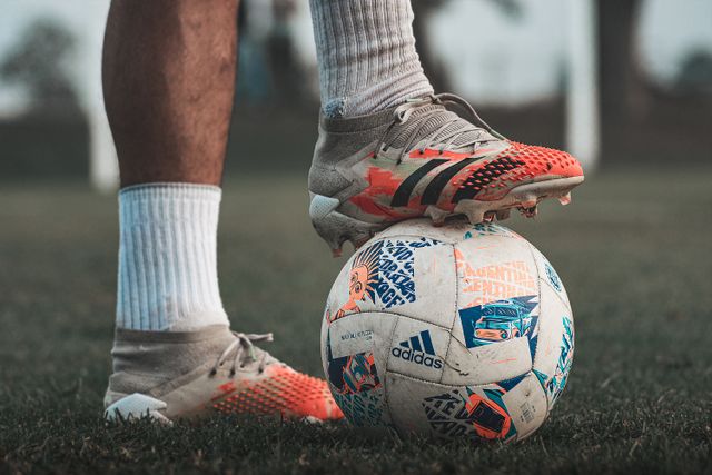 man standing with a foot on a football while wearing mucky football boots